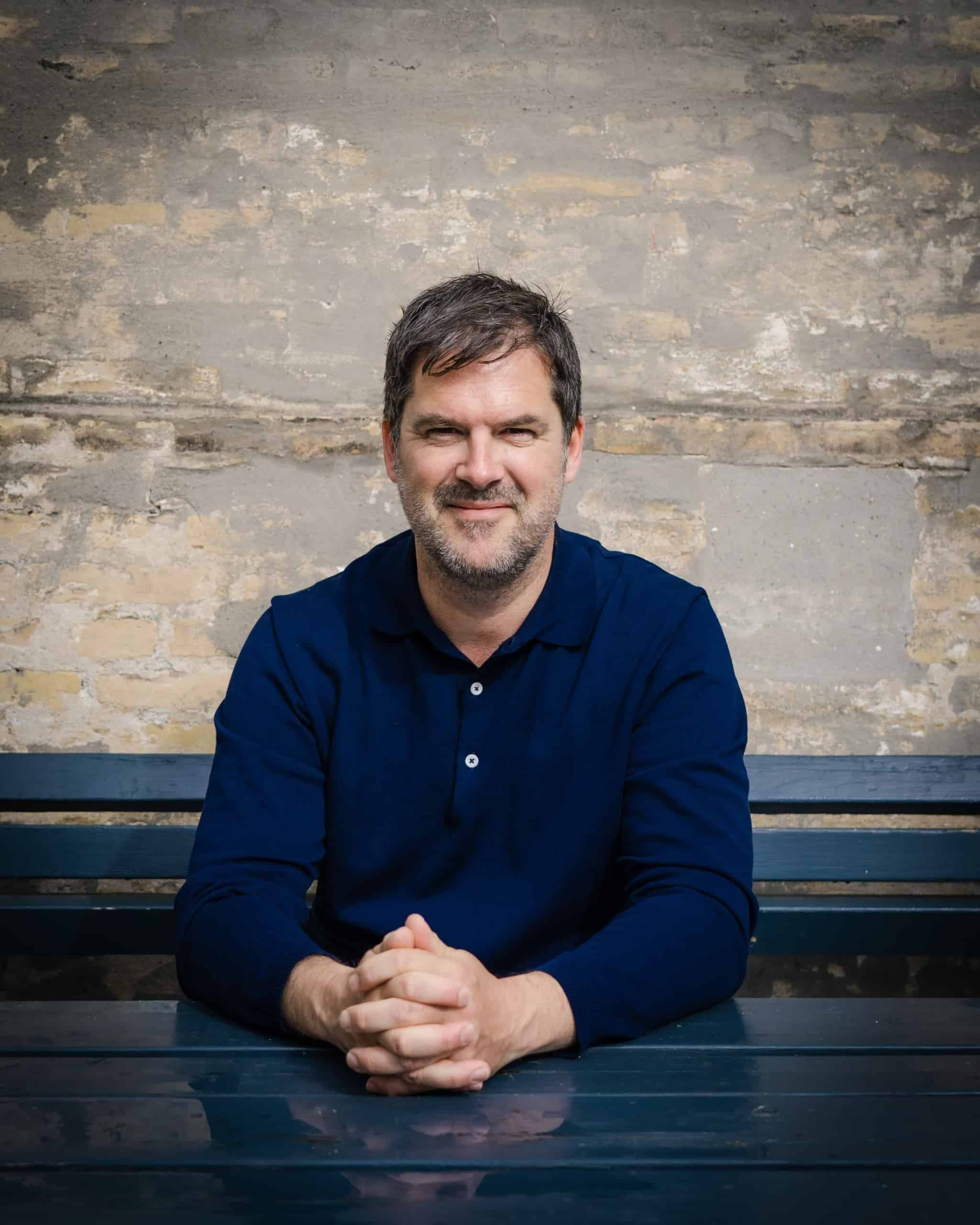 Eskil Holten sidder ved et bord foran en murstensvæg